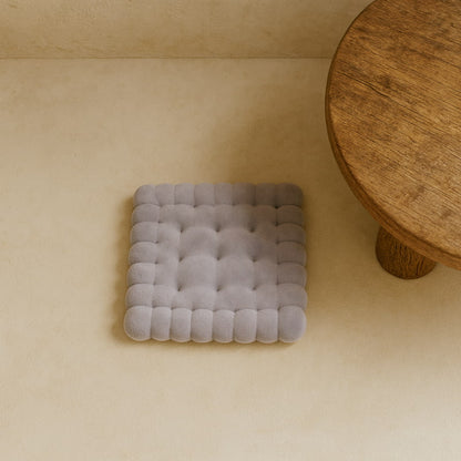 Gray thick floor cushion on a beige floor with a wooden table in the corner