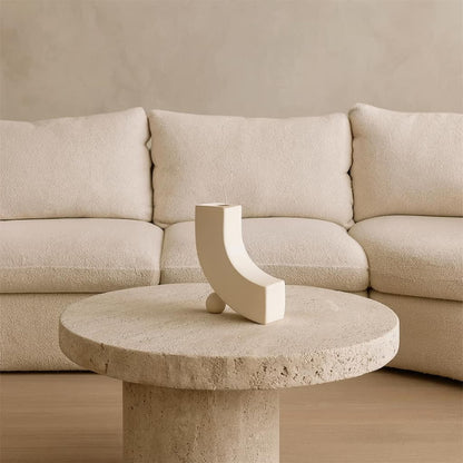 Beige stone table with a decorative unique white designer vase in front of a beige sofa.