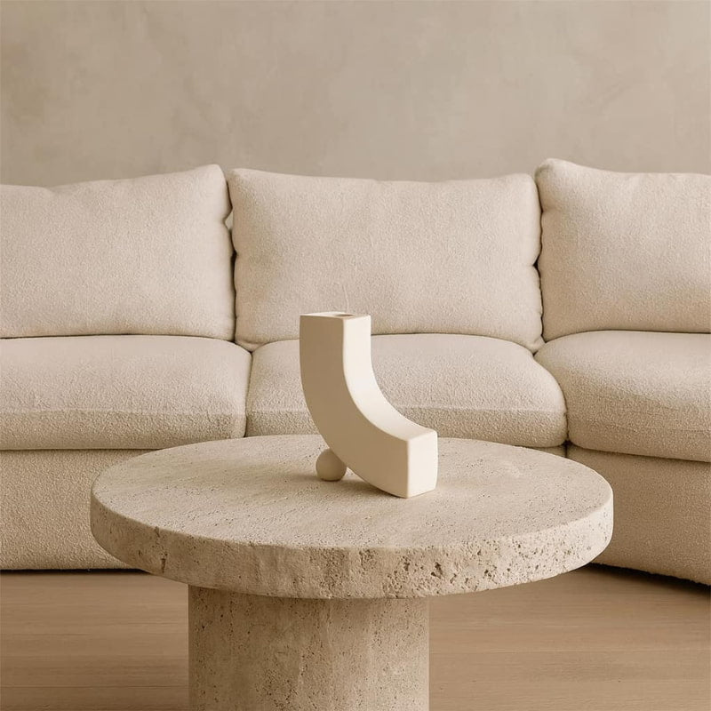 Beige stone table with a decorative unique white designer vase in front of a beige sofa.