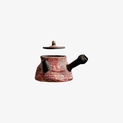 Ceramic vintage teapot with red glaze and black accents on a white background