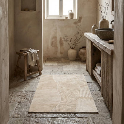 Natural wabi sabi bathroom with wooden bench, rug, and decorative vases.