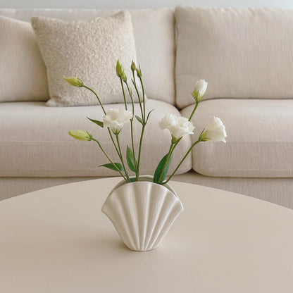 Shell-shaped wabi sabi style pot with white flowers on a coffee table in front of a beige sofa.