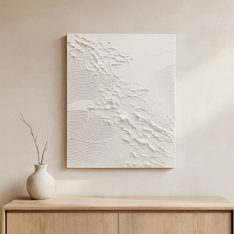 Wabi sabi textured art​ on a wall above a wooden cabinet with a vase.
