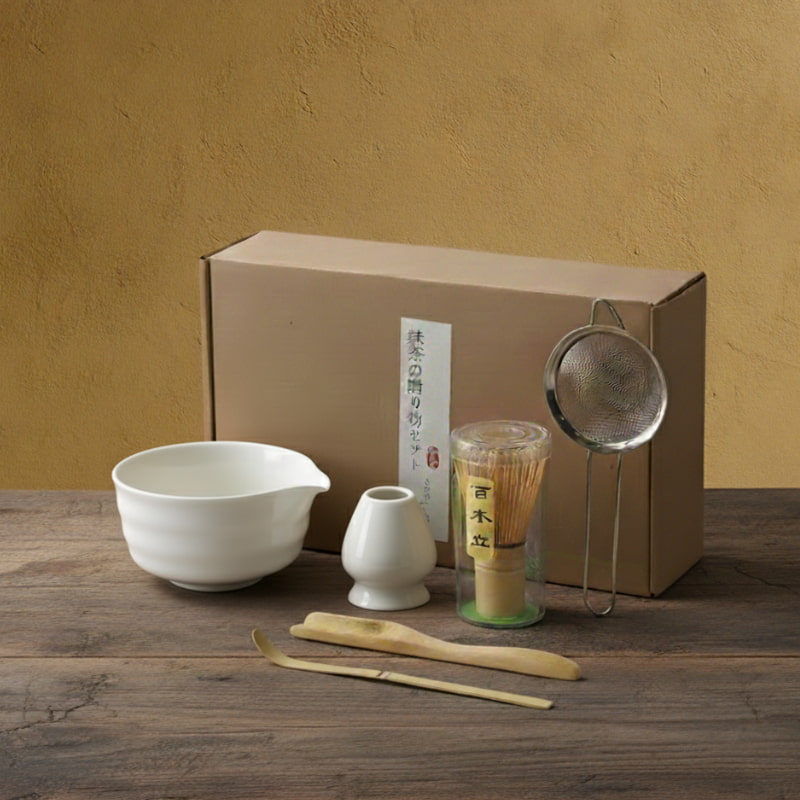 Tea-making set with bowls, strainers, whisk utensil​ and a box on a wooden surface.