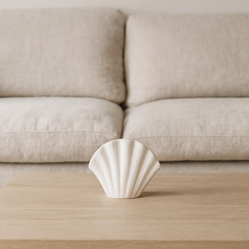 White ceramic vase shell on a wooden table with a beige sofa in the background