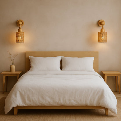 Neatly made bed with white bedding in a bedroom setting with wicker wall lamp shade​.