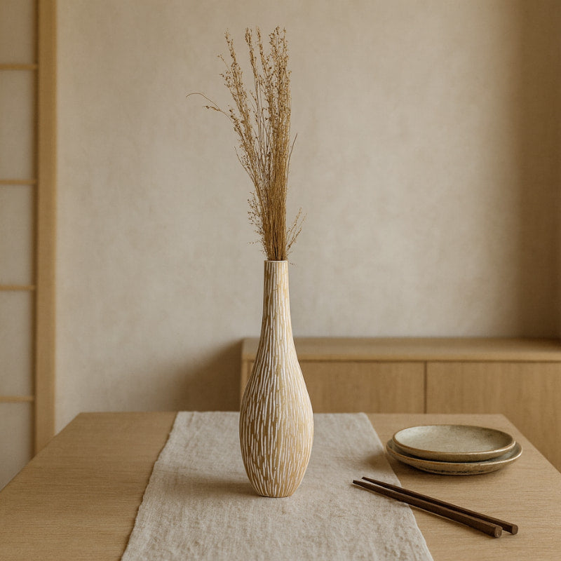 Wood carved flower vase with dried plants on a table with plates and chopsticks in a minimalistic setting.