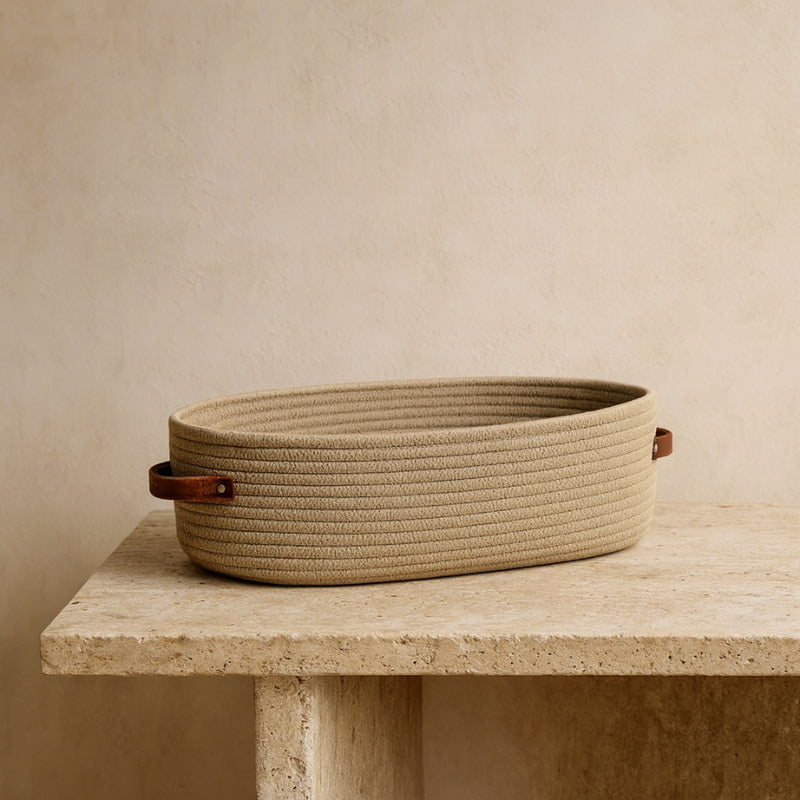 Beige woven basket with leather handles on a wooden table against a beige wall