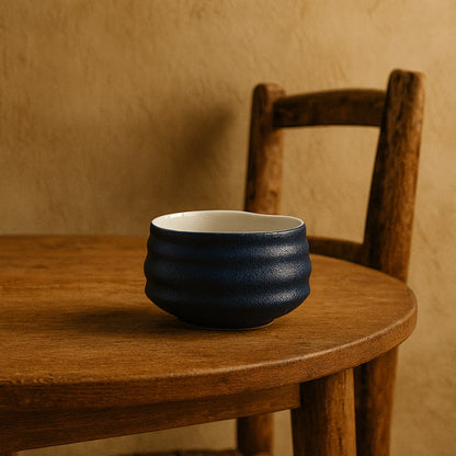 Blue zen matcha bowl​ on a wooden table with a wooden chair in the background